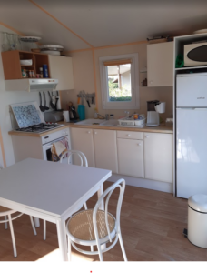 Compact kitchen with white cabinets, a small table and chairs, gas stove, sink, and a window above the counter of a cozy home kitchen. For accessibility, this conveys the layout and main features without focusing on decor details.