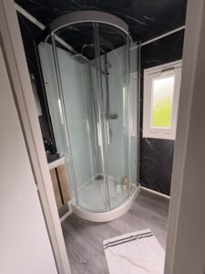 Curved glass corner shower enclosure in a modern bathroom with black marble walls and a small window.