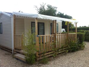 Beige mobile home with a wooden deck and a long white canopy shade along the front.