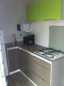 Compact kitchen with lime green wall cabinets, brown lower cabinets, and a stainless sink on a dark countertop.