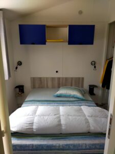 Small bedroom with a single bed, blue wall cabinets above and a yellow towel in a central cubby, minimal décor, compact cabin aesthetic