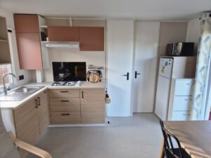 A compact kitchen with light wood cabinets, cream countertops, a gas stove, and a sink under a window; a fridge and microwave are in the corner.